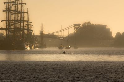 Ein Kanufahrer in goldener, nebliger Morgenstimmung im Hafen. Im Hintergrund die KW-Brücke, am Bontekai liegen Großsegler.